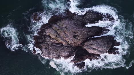 a birds-eye drone video looking down towards some large rocks above the ocean