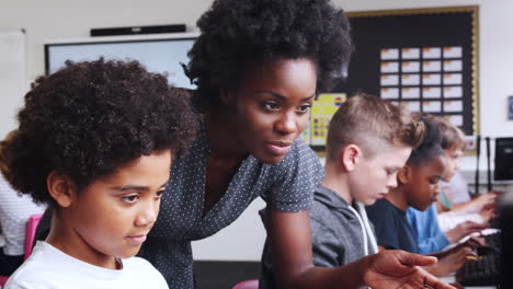 teacher helping male pupil in line of high school students working at screens in computer class