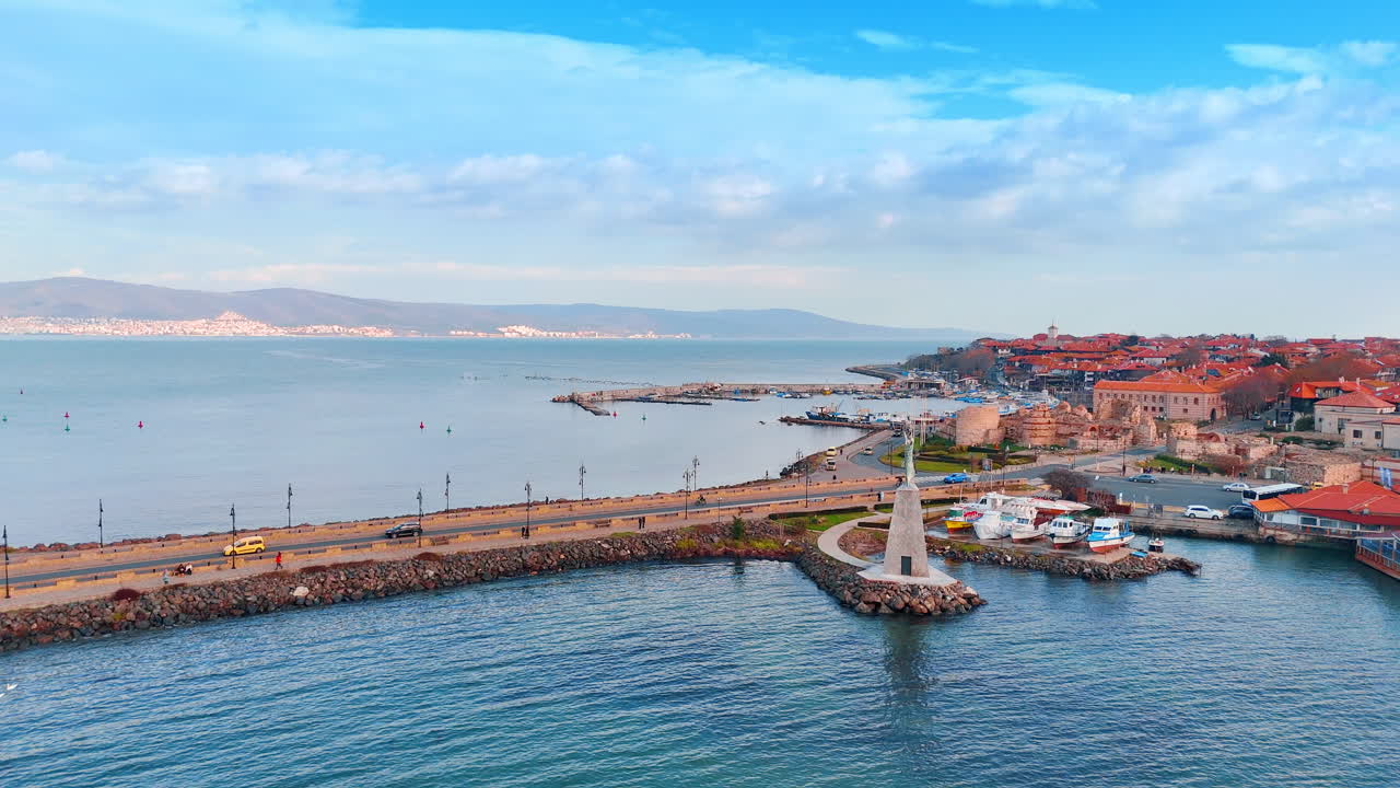 Vista aerea di una strada a ponte che collega una città costiera. Ampia inquadratura di una lunga strada rialzata con auto sull'acqua blu che conduce a una storica città di mare con rovine.