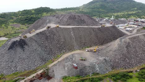 aerial view of a mountain of debris or a rubble heap with dumper trucks unloading more rock debris from a tunnelling project in a hilly region impacting the local ecology and terrain