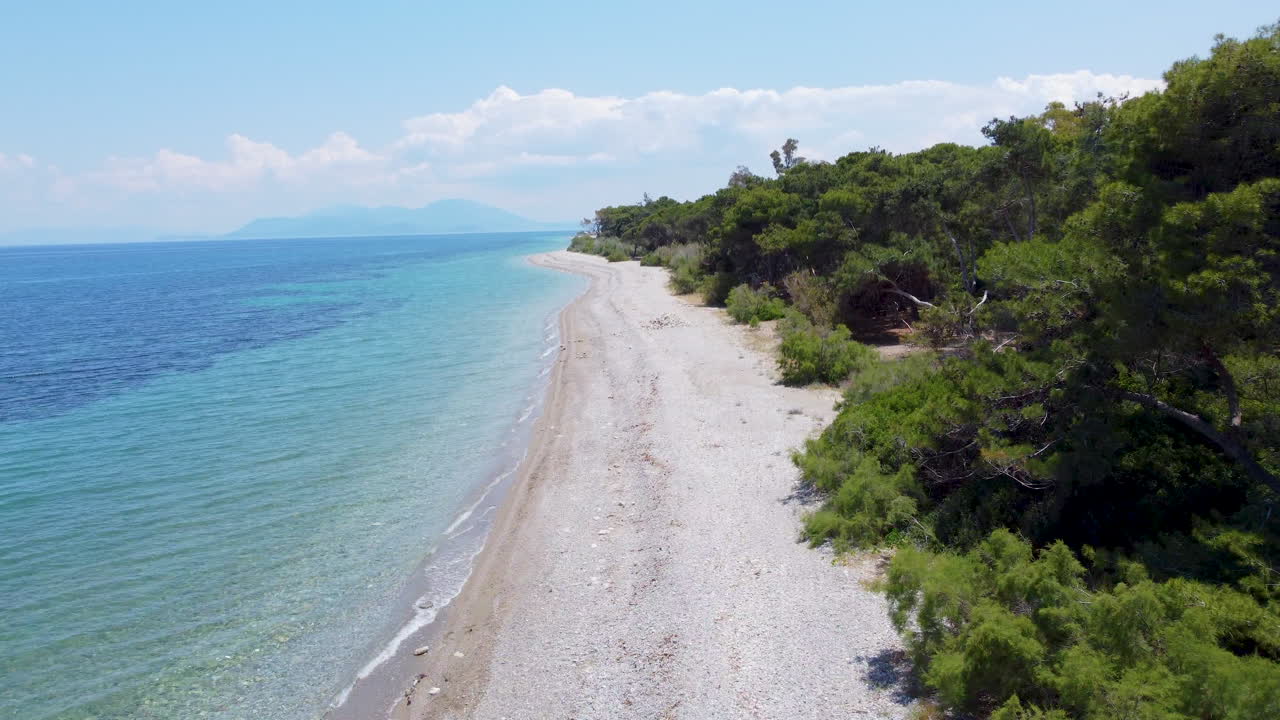 A drone flies parallel to an empty, pristine beach along the Greek coastline