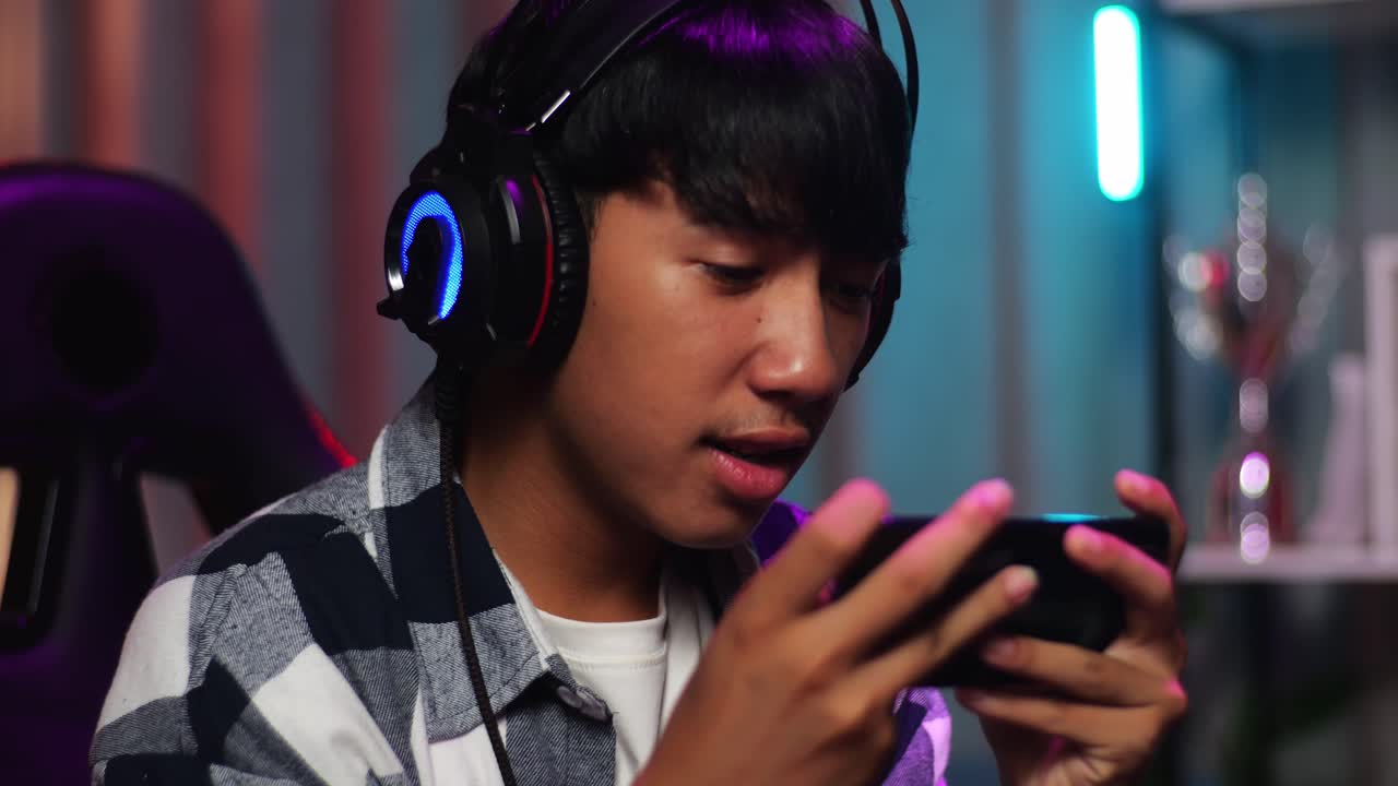 흥분한 아시아 십대 소년 게이머가 스마트폰으로 비디오 게임을 하는 동안 승리를 축하하고 춤을 추고 있습니다.