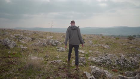 Following-male-hiker-walking-across-rocky-terrain-with-sparse-vegetation,-Israel