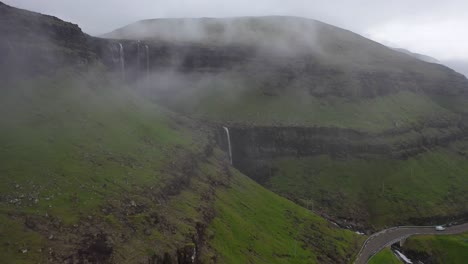 Fossá-Waterfall-on-Faroe-Islands-coastline,-aerial-dolly-reveal-through-clouds