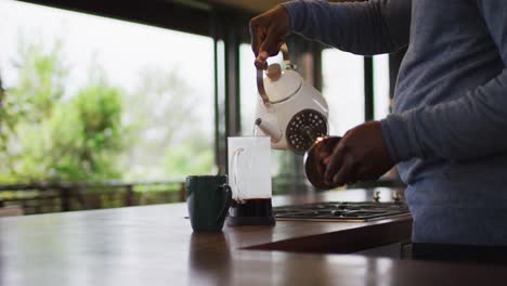 sección media de un hombre mayor afroamericano en la cocina haciendo café en una olla
