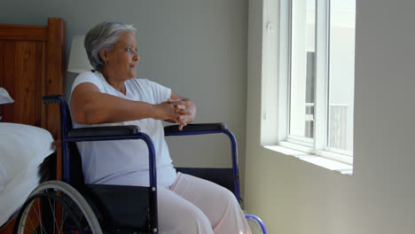 Side-view-of-handicap-senior-black-woman-sitting-on-wheelchair-near-window--in-bedroom-at-home-4k