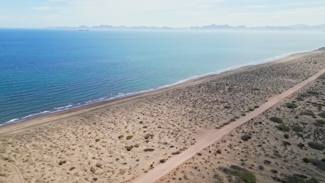 Remote beach with dry sand, desert plants and blue sea, El Mogote, La Paz, Mexico