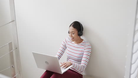 Glückliche-Biracial-Frau,-Die-Auf-Der-Treppe-Sitzt-Und-Kopfhörer-Und-Laptop-Benutzt,-Zeitlupe