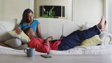Happy-biracial-couple-on-sofa-with-laptop-and-talking