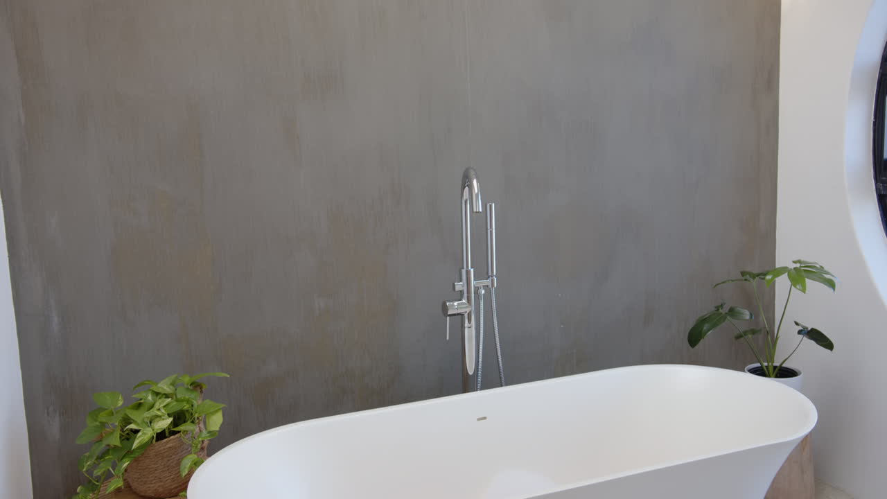 Modern bathtub with sleek faucet and green plants in minimalist bathroom, copy space
