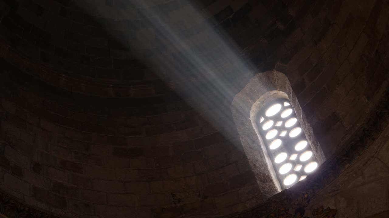 primer plano de una luz brillante que brilla a través de una antigua ventana de la iglesia que se transmite a través de la oscuridad de la catedral