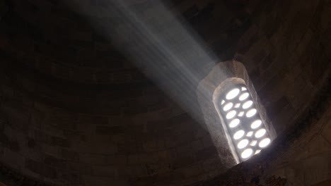 Close-up-of-a-bright-light-shining-through-an-old-church-window-beaming-through-the-darkness-of-the-cathedral