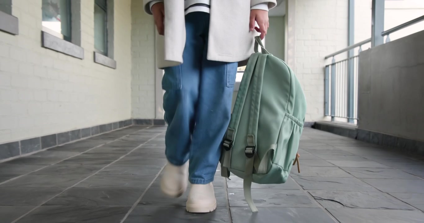 African American teenage female walking toward camera along corridor, carrying mint-green backpack