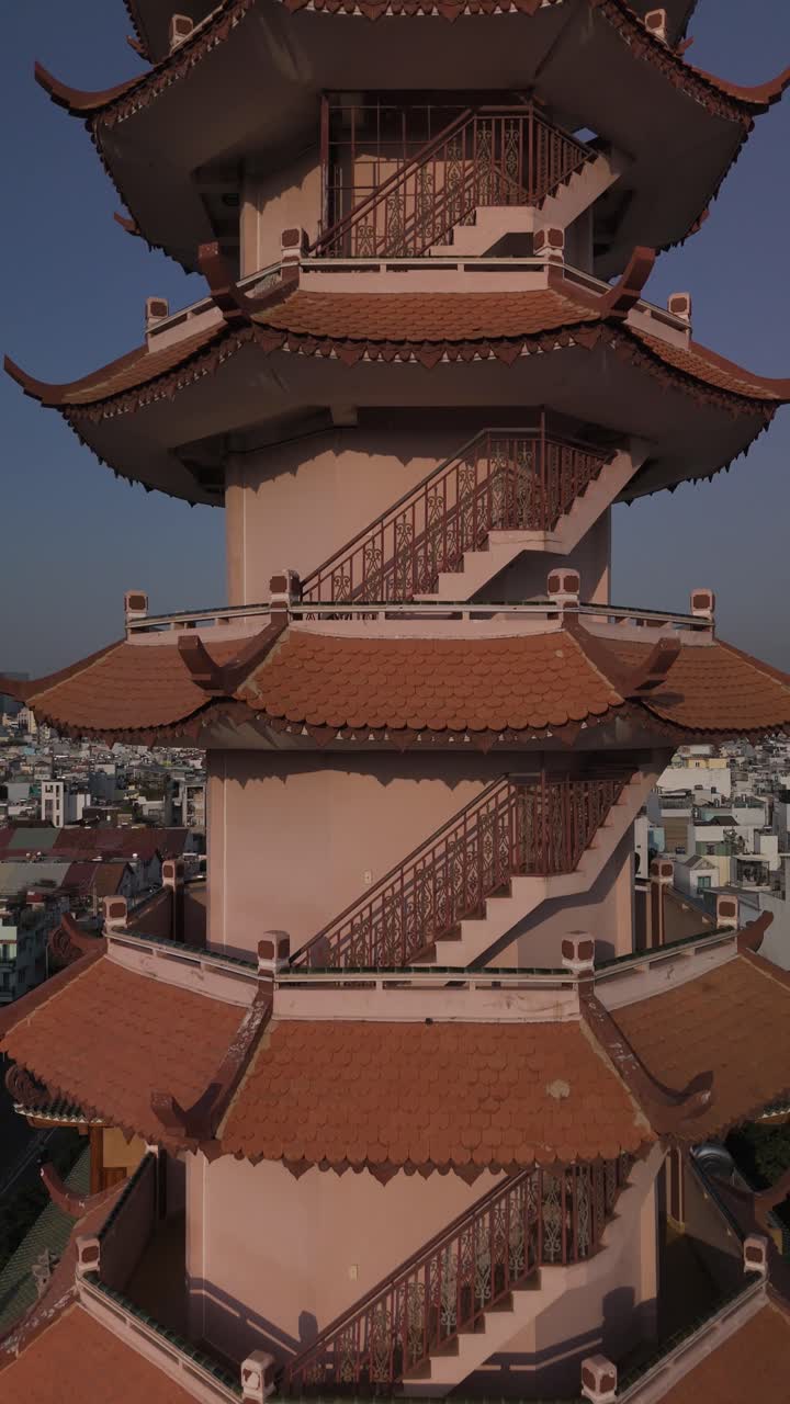 Buddhist Pagoda prayer tower in dense urban area in sunny late afternoon light. Drone camera flies up the side of the building past the top revealing urban sprawl in Vertical video format