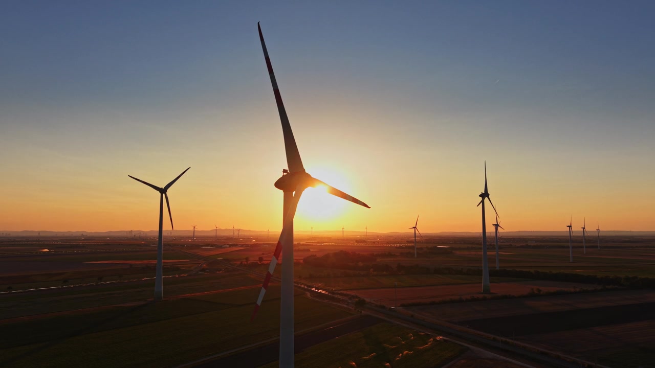 Wind turbines stand against the sunset in a rural landscape
