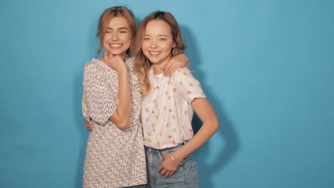 two happy women friends posing in front of a blue background