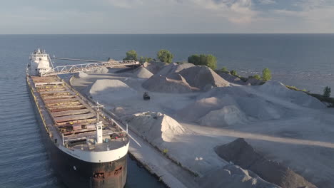 huge industrial ship at the sand quarrying site surrounded by the calm sea in kingsville, ontario, canada - descending drone shot