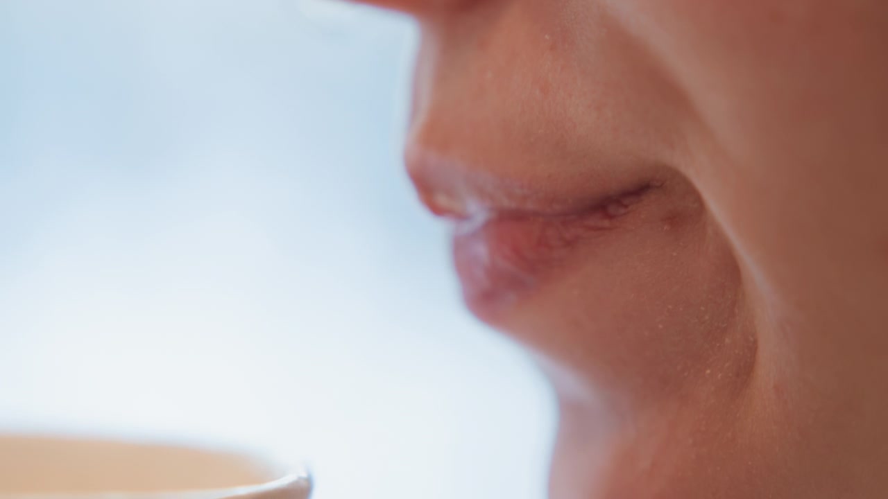 Vista ravvicinata di profilo della parte inferiore del viso mentre una persona sorseggia da un bicchiere di carta, con le labbra che toccano il bordo, dettagli della pelle morbidi e luce interna calda, creando un'atmosfera tranquilla e rilassata, comfort sensoriale e un momento intimo quotidiano.
