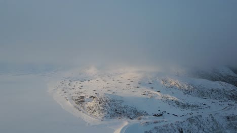 Atmospheric-drone-footage-of-frozen-mountain-lake-an-mountain-cottages-covered-in-snow-on-the-shore