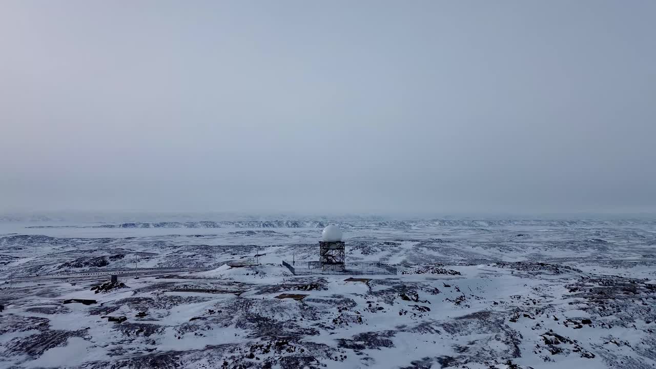 Cinematic aerial push toward a remote North Warning System radar dome in the snowy Arctic tundra near Iqaluit, showcasing isolated defense infrastructure in winter