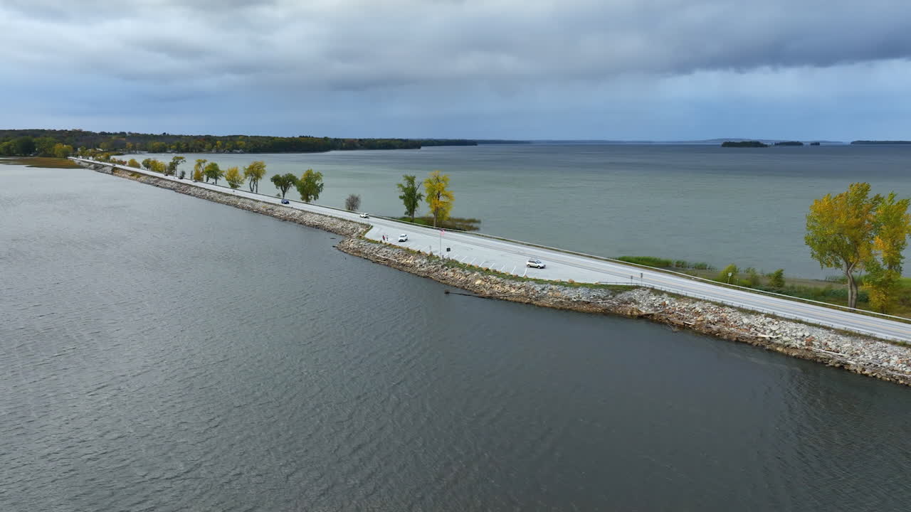 Cars riding by the highway built along the lake. Waterscape of Lake Champlain, Vermont, New England, USA. Grey day on the lake.