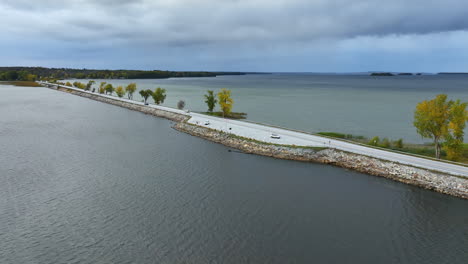 cars riding by the highway built along the lake. waterscape of lake champlain, vermont, new england, usa. grey day on the lake.