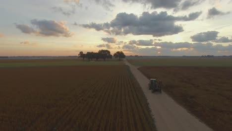 farmer driving large industrial commercial farm equipment along dirt road at sunrise