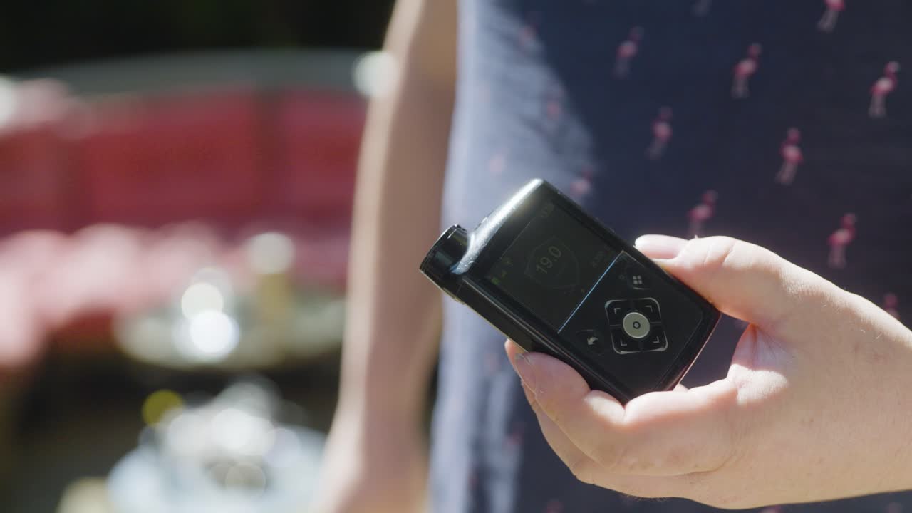 A man's hand holding and adjusting a digital insulin pump device. Shot in daylight, focusing on healthcare technology in daily life.