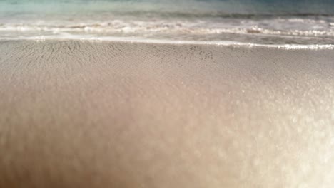 water runs out into the jade green atlantic ocean as waves gently lap and crash against the sparkling, golden summer sand