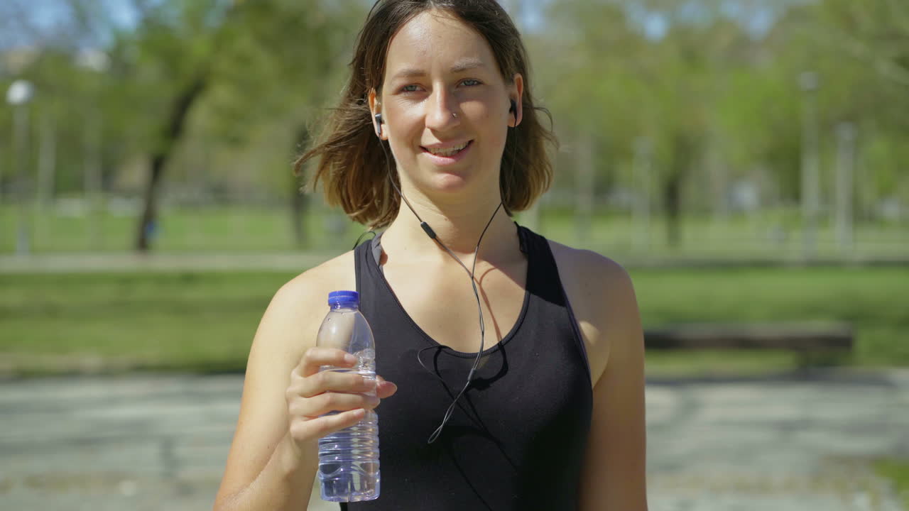 mujer joven sonriente caminando en el parque y escuchando música