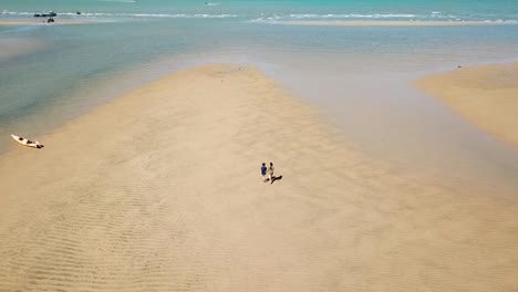 Vista-Aérea-A-Vista-De-Pájaro-En-Pareja-Caminando-En-La-Playa-Hacia-El-Mar-En-Marea-Baja