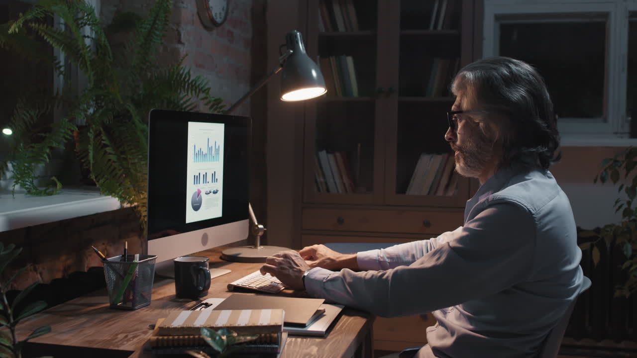 Mature Man Working on Computer in Home Office at Night
