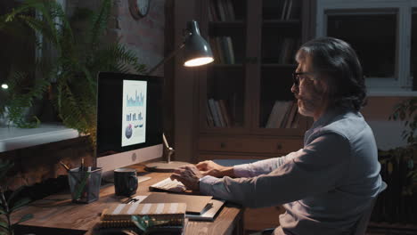 mature man working on computer in home office at night
