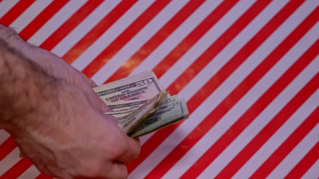 Närbild av man som räknar pengar i amerikanska dollar på röd och vit julbakgrund