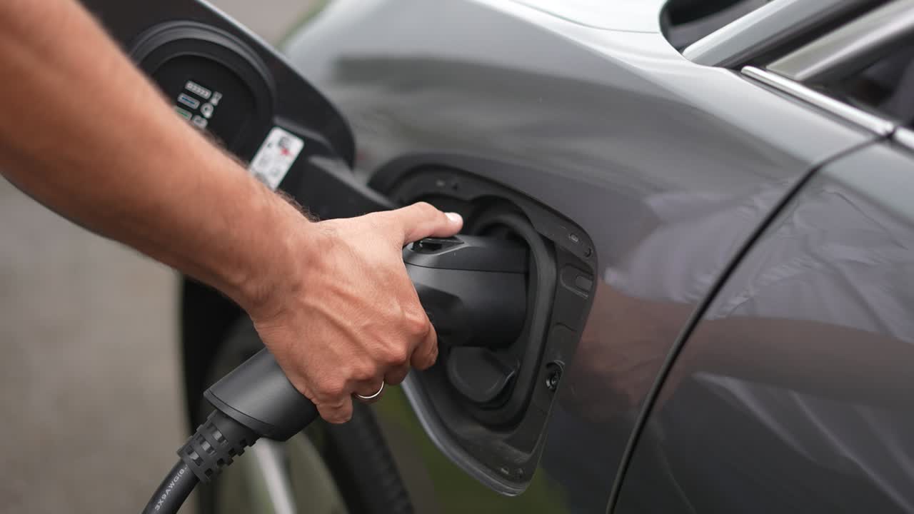 Adam şarj cihazıyla elektrikli araba şarj ediyor.