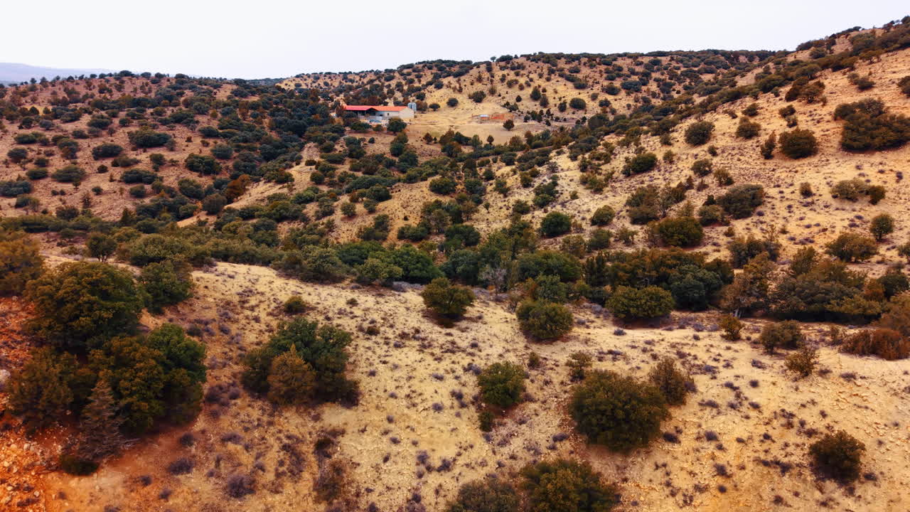 Vista aerea di un edificio agricolo rurale tra le colline aride spagnole. Piccolo complesso agricolo con tetto rosso situato tra colline secche e arbusti verdi nella regione di Teruel, Spagna.