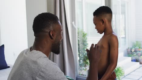 padre afroamericano ayudando a su hijo a vestirse en el dormitorio