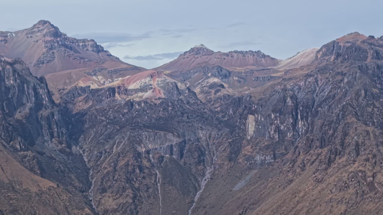 Panoramica ravvicinata con drone delle imponenti cime del Canyon del Colca che si ergono dalla base del canyon. Sabbia rossa ricca di ferro e depositi di zolfo giallo rivestono le scogliere frastagliate, creando un paesaggio surreale e ricco di minerali.