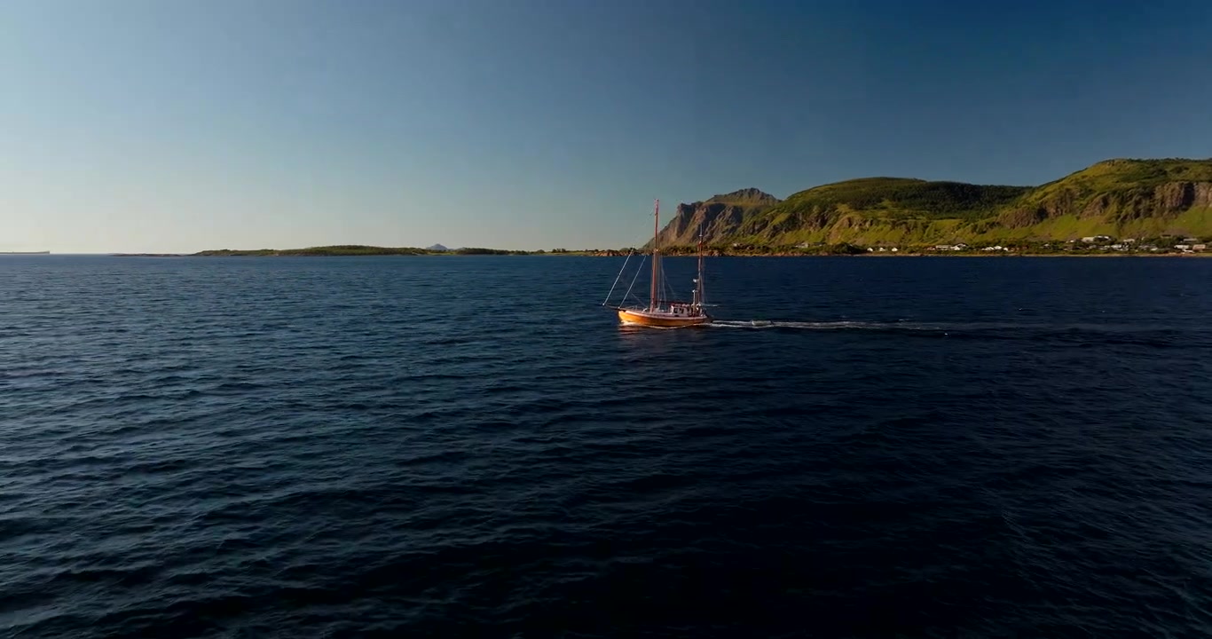 Norveç'teki Lofoten Adaları'nın görkemli kayalıklarıyla çevrili sakin fiyortta seyreden yelkenli tekne. Mavi sular üzerinde geriye doğru uçan havadan drone, metin alanı