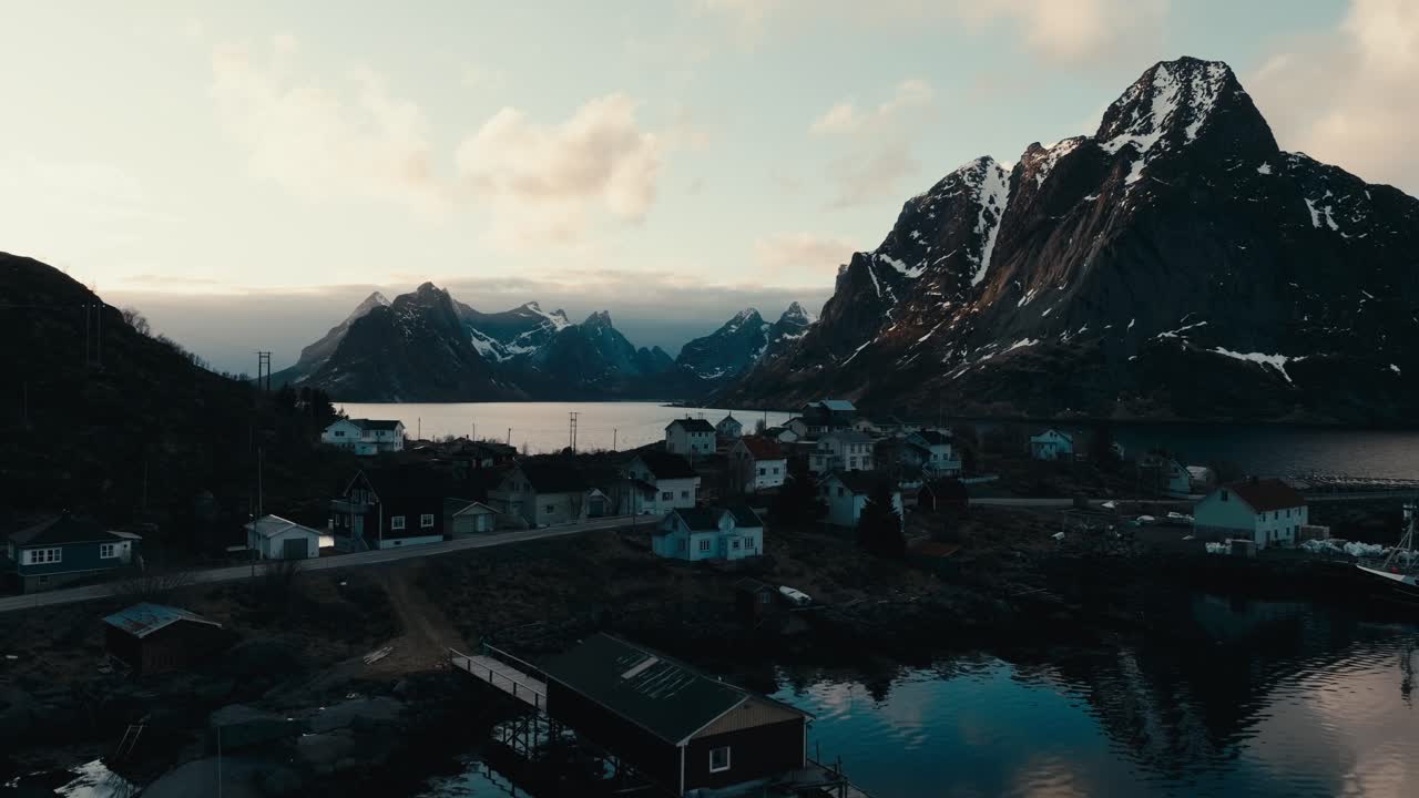 Reine, Isole Lofoten, Nordland, Norvegia - Un sereno villaggio costiero circondato da maestose montagne innevate riflesse nell'acqua calma - Ripresa aerea con drone