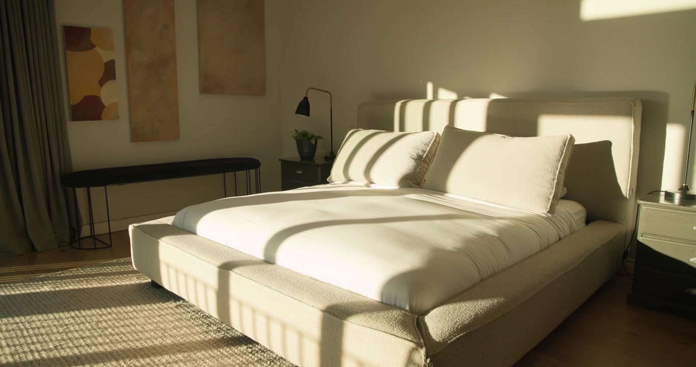 La luce del sole forma strisce sul letto attraverso la finestra mentre la telecamera si muove per evidenziare i cuscini.
