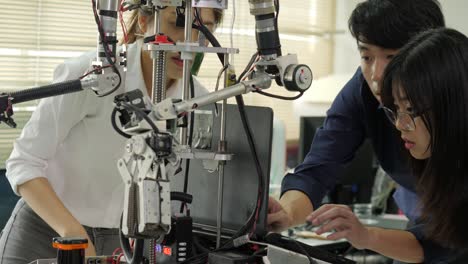 team of robotics engineer works with robot, assembling and testing robotics responses with laptop computer in workshop. people with technology or innovation concept.