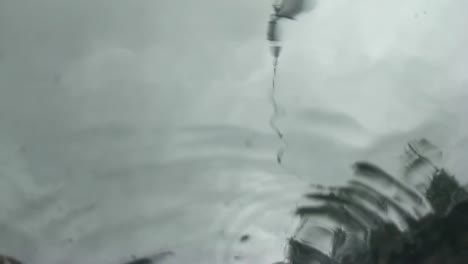 slow motion abstract view of rain drops landing on glass as seen from below, underneath, gray sky