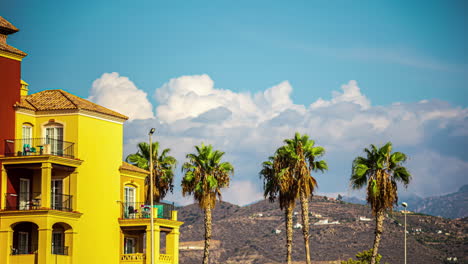 sunny day view of palm trees and colorful buildings with mountains in the background