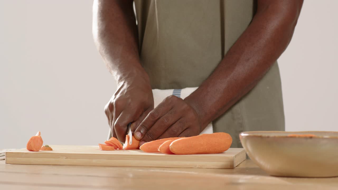 African American man placing carrots on cutting board, picking up chef's knife, slicing for meal