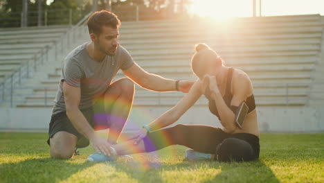 Junge-Joggerin,-Die-Auf-Grünem-Gras-Sitzt-Und-Schmerzen-Im-Bein-Hat,-Die-Während-Des-Trainings-Im-Stadion-An-Einem-Sonnigen-Tag-Verletzt-Wurden-1