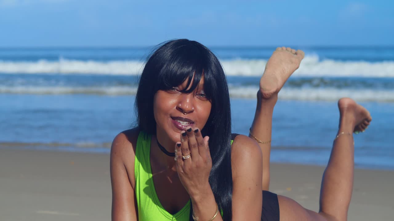 Dikelilingi oleh pohon kelapa yang condong, seorang wanita ber bikini ramping hijau limau dan hitam menatap cakrawala biru tak berujung.