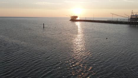 Aerial-panoramic-view-of-a-trabucco-silhouette,-a-traditional-fishing-machine,-on-the-italian-seashore,-at-sunset