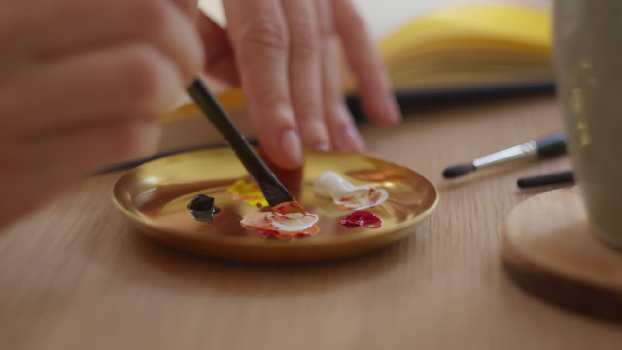 パレットで色を混ぜるアーティストの手のクローズアップ。