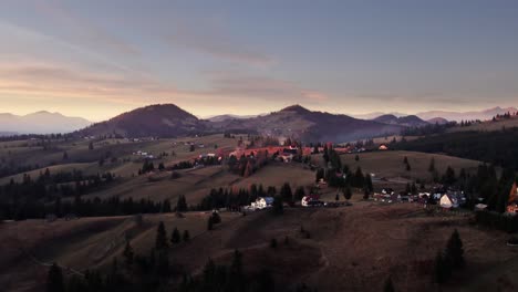 Revelación-Aérea-Del-Pintoresco-Pueblo-En-La-Colina-De-La-Montaña-Alpina-Al-Atardecer,-Transilvania